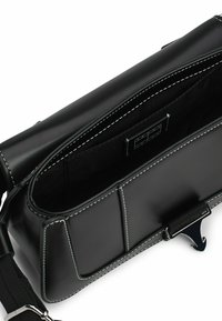 Bolso de piel negra con costuras blancas en contraste, un interior espacioso con dos compartimentos y un cierre de hardware plateado seguro.