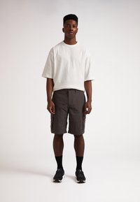 T-shirt blanc oversized, short cargo gris avec poches latérales, chaussettes noires et chaussures de sport. Tissu doux, coupe décontractée et design pratique.