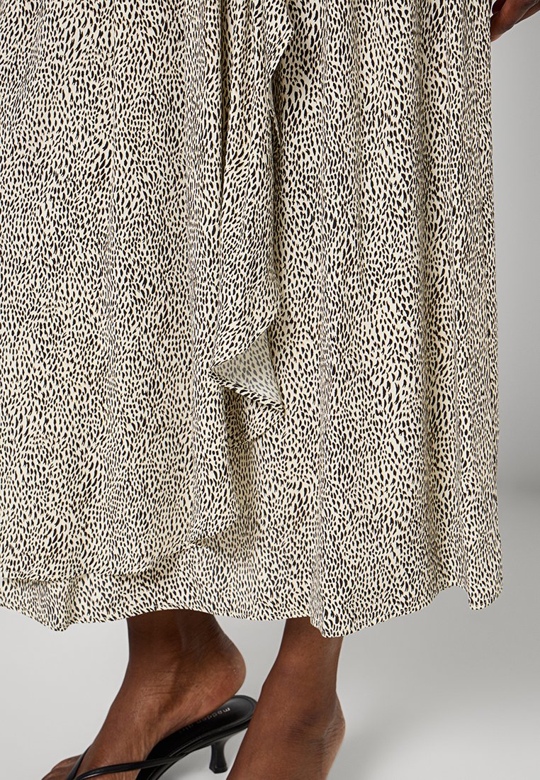 Czarna i beżowa sukienka w wzory z teksturowanej tkaniny, o luźnym kroju i długości spodni spadającej poniżej kolan. W zestawie czarne klapki.