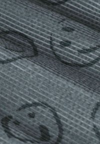 Grijze stof met textuur, gekenmerkt door een herhalend patroon van glimlachende gezichten in zwarte omlijning, met subtiele ribbels die door de stof zichtbaar zijn.