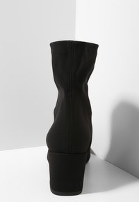 Botín negro hasta el tobillo hecho de una tela elástica, con un diseño afinado, tacón bajo en bloque y costuras sin interrupciones en la parte trasera.