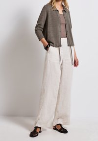 Cardigan vert olive léger avec un col à revers et une fermeture à boutons, associé à un pantalon large en lin couleur crème et des sandales noires.