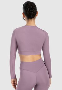 Lilafarbener langärmliger athletischer Crop-Top mit enganliegendem Design und glatter Textur. Verfügt über einen breiten Bund und wird mit passenden hochtaillierten Leggings kombiniert.