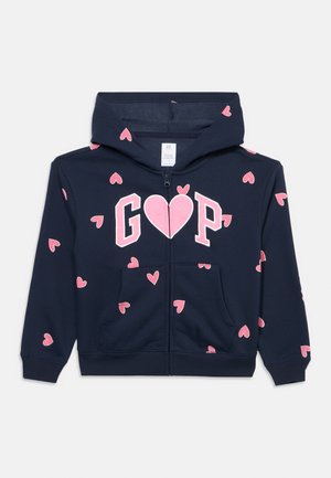 Γαλάζιο φούτερ με φερμουάρ και ροζ καρδιές, με το λογότυπο "GAP" σε ροζ γράμματα, όπου η καρδιά αντικαθιστά το "A", με μπροστινές τσέπες και κουκούλα.