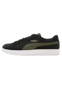 Zapatillas sintéticas negras con detalles en verde oliva, suela de goma blanca, punta redonda y diseño con cordones que presenta el logotipo de Puma en el lateral.