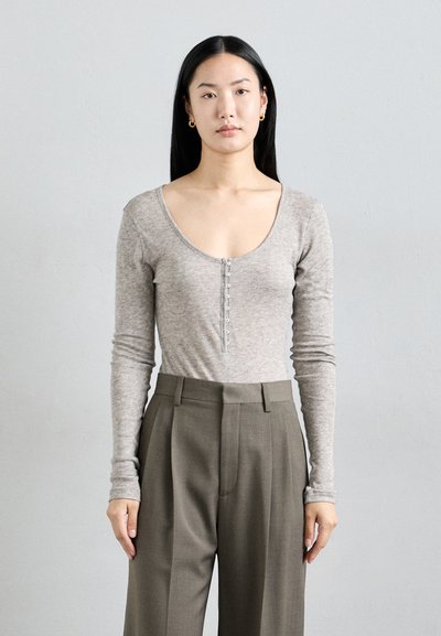 Haut à manches longues gris chiné avec un décolleté plongeant et des boutons, associé à un pantalon taille haute en olive ajusté.