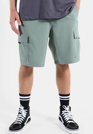 Homme portant un short cargo vert, des baskets montantes noires avec des lacets blancs et des chaussettes noires à rayures blanches.