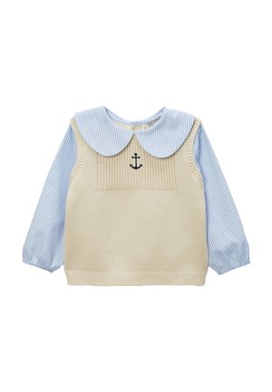 Pull sans manches beige en maille porté par-dessus une chemise à manches longues bleu clair et blanc à rayures, avec un grand col arrondi et une petite broderie noire en forme d'ancre.