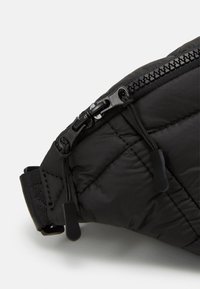 Czarna wyściełana torba na ramię z teksturowaną powierzchnią, wyposażona w górny suwak i uchwyty do otwierania. Regulowany pasek zapewniający pewne dopasowanie.