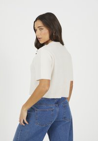 Skórzany, prążkowany sweter w kolorze kremowym z krótkim rękawem. Połączony z niebieskimi dżinsami z wysokim stanem i tylnymi kieszeniami.