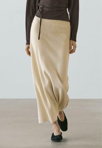 Beiger Maxi-Rock aus Wollmischung mit elastischem Bund und dezentem Fall, kombiniert mit einem dunklen langärmligen Oberteil und schwarzen flachen Schuhen.