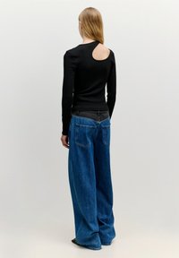 Schwarzes Langarmtop mit einem auffälligen Ausschnitt auf der Rückseite, kombiniert mit lockeren blauen Jeans aus Denim im klassischen Fünf-Taschen-Design.