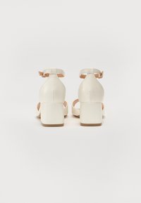 Vita klacksandaler med blockklack, justerbar ankelrem, slät lädertextur, öppen tå-design och beige innersula.
