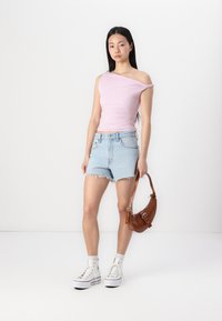 Top asimétrico de color rosa claro con detalles recogidos, pantalones cortos de denim azul con dobladillo desflecado, bolsa de cuero marrón y zapatillas altas blancas.