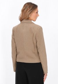 Giacca marrone in misto lana con design strutturato, colletto a revers e silhouette fitted, caratterizzata da maniche lunghe e una texture liscia.