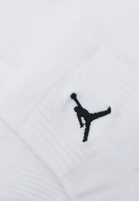 Sosete atletice albe, cu un logo Jumpman brodat de culoare neagră. Textura este ribbed și netedă, având o manșetă întărită pentru confort.