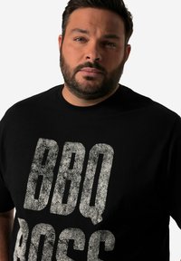 Czarna bawełniana koszulka z dużym, teksturowanym białym napisem "BBQ BOSS" w wyraźnej czcionce. Krótki rękaw i okrągły dekolt.