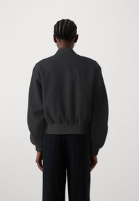 Zwarte sweatshirt met een ontspannen pasvorm, geribbelde onderkant en manchetten, met een eenvoudig ontwerp en zachte textuur. Draagt met donkere broek.