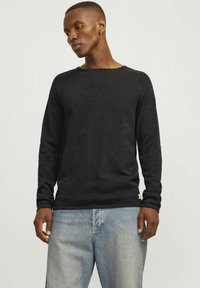 Maglione nero a maniche lunghe con lavorazione a maglia testurizzata, scollatura rotonda e polsini a coste. Abbinato a jeans azzurri chiari.