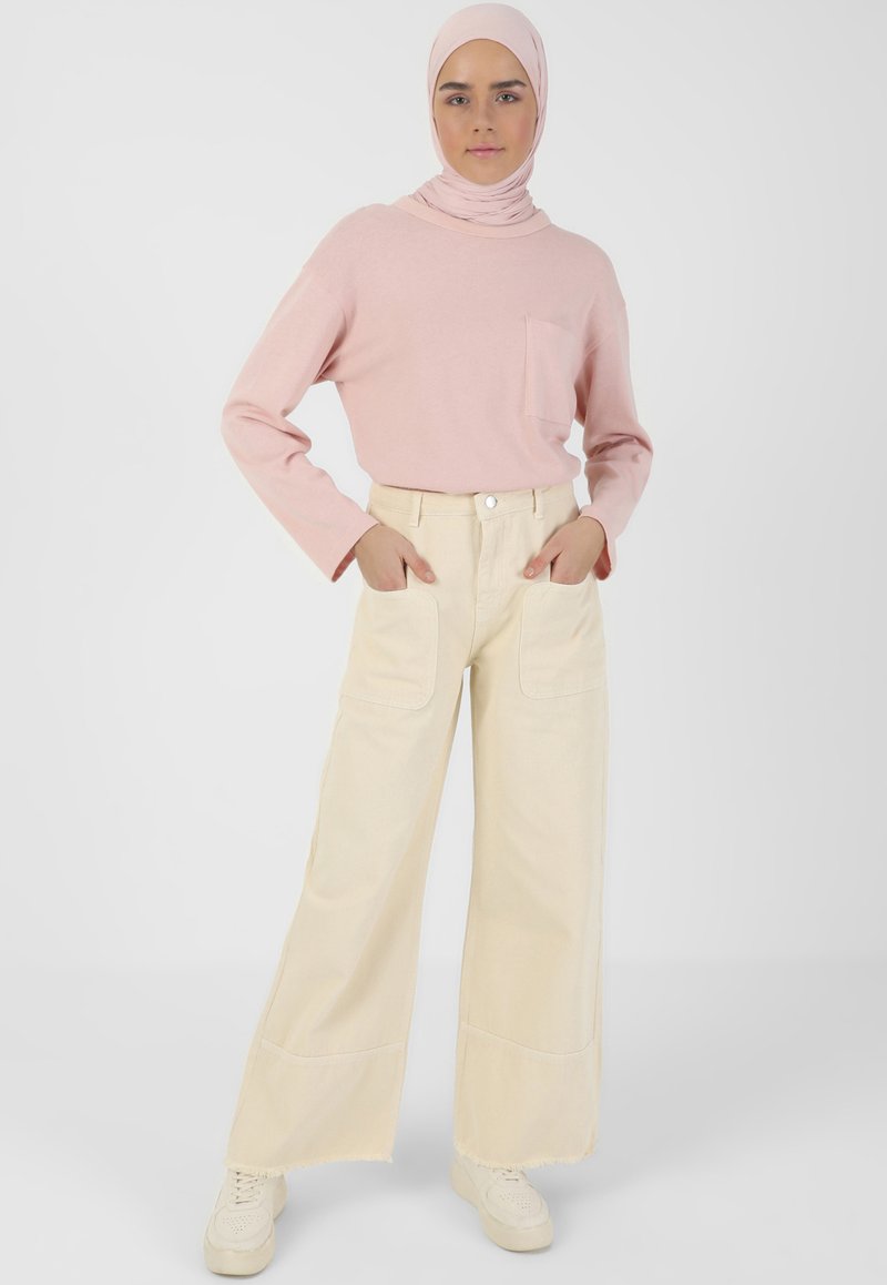 Maglietta rosa chiaro a maniche lunghe con tasca, abbinata a pantaloni ampi color crema e sneakers bianche. Tessuto morbido con vestibilità rilassata.