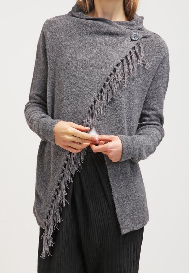 Šedý pletený kardigan s rolákem, zdobený diagonálním třásňovým akcentem a bočním zapínáním na knoflík. Měkká textura, uvolněný střih.