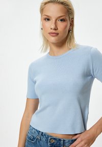 T-shirt azzurro chiaro in maglia a coste con maniche corte e scollatura a girocollo. Il tessuto ha una texture liscia e presenta una vestibilità cropped. Indossato con denim.