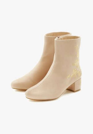 Beige Knöchelstiefel aus weichem Material mit spitzem Zehenbereich und kleinem Blockabsatz. Besticktes Blumendesign in Gold auf der Außenseite.
