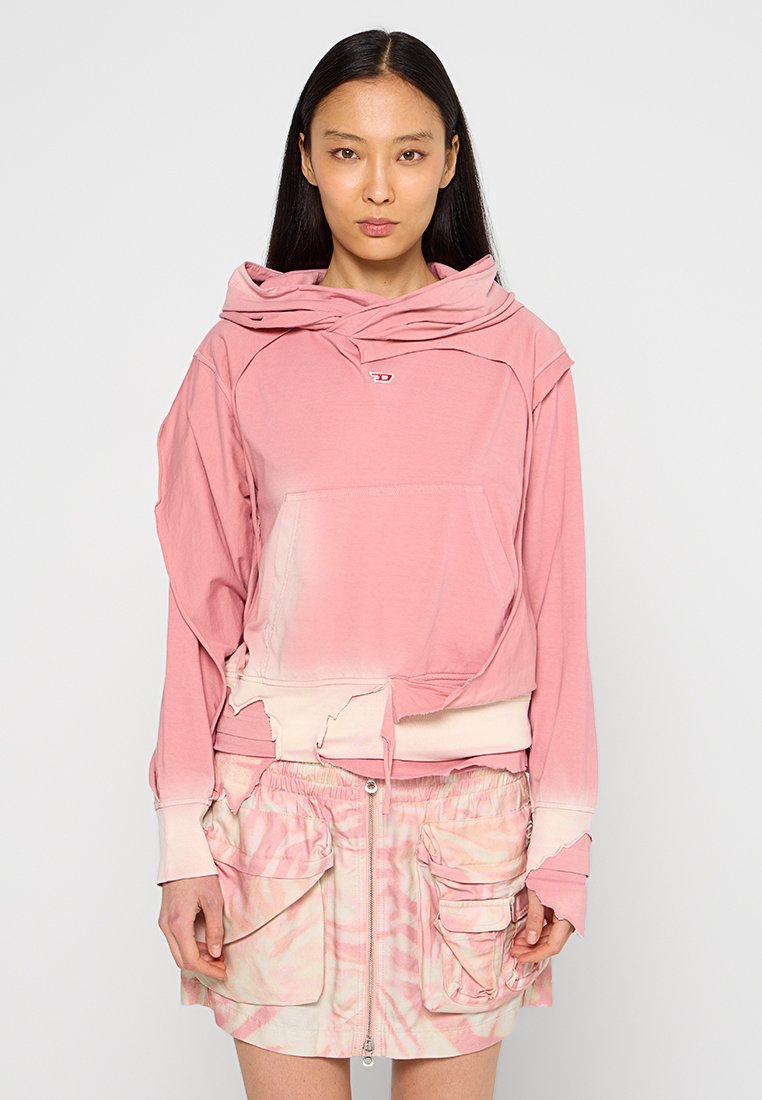 Helles rosa Übergröße-Hoodie mit abgerundetem Saum, ausgestattet mit einer Kängurutasche und einer geschichteten Kapuze. Kombiniert mit einem pastellfarbenen Tie-Dye-Reißverschlussrock mit Taschen.