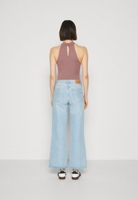 Hnědý halter bodysuit s detailem otvoru, v kombinaci s světle modrými širokými džínami a černobílými teniskami.