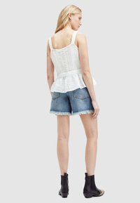 Top peplum blanco con tela texturada y detalles de encaje, combinado con shorts de mezclilla claros con dobladillo deshilachado. La modelo lleva botas negras hasta el tobillo.