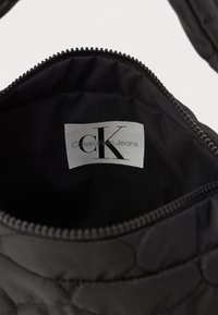 Zwarte gevoerde totebag interieur met een ritssluiting, met een label waarop "Calvin Klein Jeans" staat en een logo in het midden.