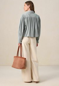Blouse bleu clair avec détail de dos froncé, pantalon large crème, et sac tote tissé marron avec un motif à rayures diagonales.