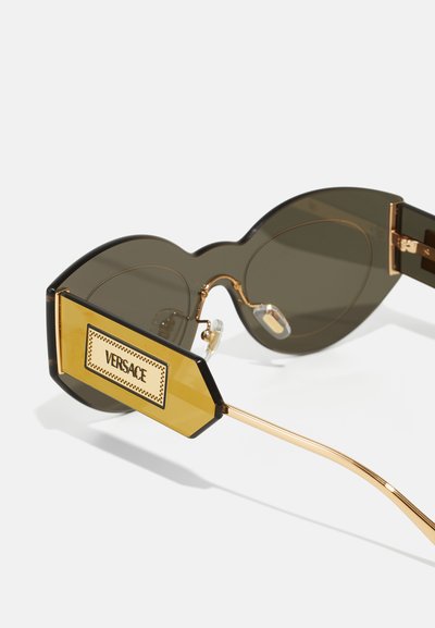 Versace prillid tumedate läätsedega, üleuuritud mustad raamid ja kuldne geomeetriline aksent käepidemetel, kus on kirjas brändi nimi.
