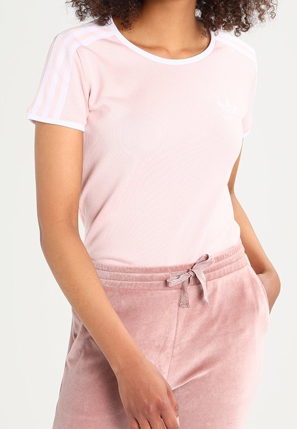 T-shirt en maille rose avec des bordures blanches et trois bandes blanches sur les épaules, associé à un pantalon en velours rose clair avec une taille à cordon.