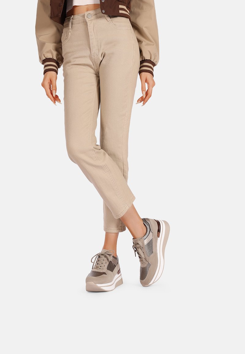 Pantaloni beige a vita alta con un sottile motivo testurizzato, abbinati a sneaker multicolori con dettagli in rete e suede e una spessa suola bianca.