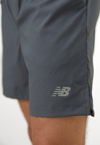 Gray athletic shorts made of lightweight material, featuring a New Balance logo on the left thigh and a side slit for mobility.