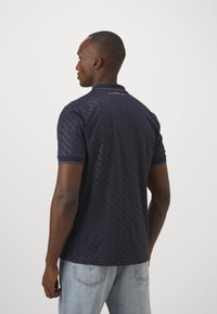 Marineblaues Poloshirt mit strukturierter Musterung, Kragen und kurzen Ärmeln. Hergestellt aus glattem Stoff mit einem kontrastierenden Besatz.