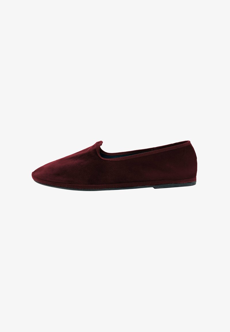 Zapato burdeos de tipo slip-on con un material de suave ante y un perfil bajo. Presenta una puntera redondeada y una suela flexible de goma negra. Textura suave.