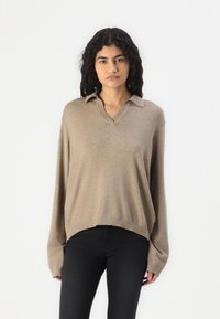 Maglione lavorato a maglia beige con scollo a V, maniche lunghe e una vestibilità rilassata. Presenta un colletto ripiegato e dettagli a coste sull'orlo.