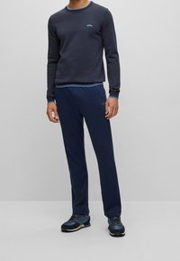 Camisa de manga larga de la marina con acentos azules y logotipo, combinada con pantalones a juego. El calzado presenta detalles en azul oscuro y gris.