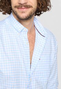 Lyseblå gingham skjorte med knaplukning og krave, der har en rød detalje ved halsudskæringen og en brystlomme. I bomuldsstof med en glat tekstur.