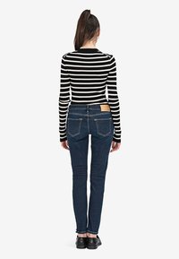 Czarna i biała w paski bluzka z długim rękawem w połączeniu z ciemnoniebieskimi, dopasowanymi dżinsami z brązową skórzaną metką z tyłu oraz widocznymi detalami przeszycia.