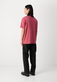 Tricou cu mânecă scurtă și guler rotund, de culoare roz pal, fabricat dintr-un material moale. Poartă-l cu pantaloni negri, moi și încălțăminte neagră.