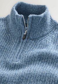 Gaiši zila adīta džemperis ar augstu apkakli un pus-izslieto dizainu. Tekstūrēts audums ar ribu detalējumu un gludu rāvējslēdzēju.