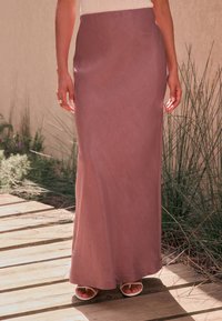 Lang, tætsiddende nederdel i mauvefarvet stof med en glat tekstur, der har en diskret glans og en lige silhuet. Båret med lyse sandaler.