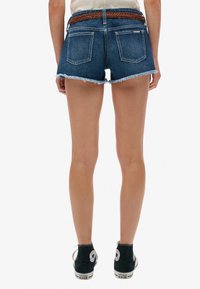 Shorts en jean avec un ourlet effiloché, couleur bleu moyen, design à cinq poches, et une ceinture tressée marron. Portés avec des baskets montantes noires.