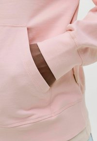 Lichtroze hoodie met een voorzak en ribgebreide manchetten. Zachte, gladde textuur met zichtbare stiksels.