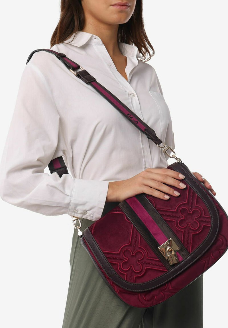Borsa a tracolla in suede bordeaux con design floreale in rilievo, un clasp dorato e una tracolla regolabile a strisce in rosa scuro e chiaro.