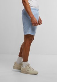 Shorts légers de couleur bleu clair avec une taille élastique et des poches latérales. Portés avec des chaussettes blanches et des baskets beiges.