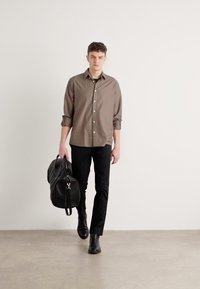 Bruine button-up shirt, zwarte fitted broek, zwarte leren duffel tas, en zwarte laarzen. Glad stof, casual ontwerp. Eenvoudige, strakke silhouet.